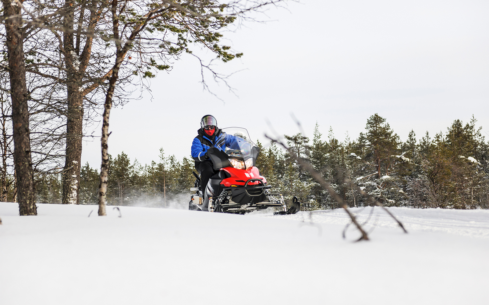 Snowmobile rider on frozen lake in winter, Lapland forest backdrop.