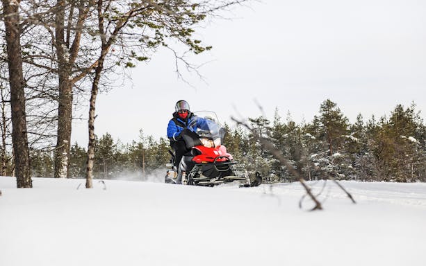 Snowmobile rider on frozen lake in winter, Lapland forest backdrop.