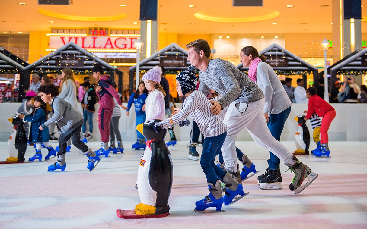 Families ice skating at Dubai Ice Rink with penguin skating aids.