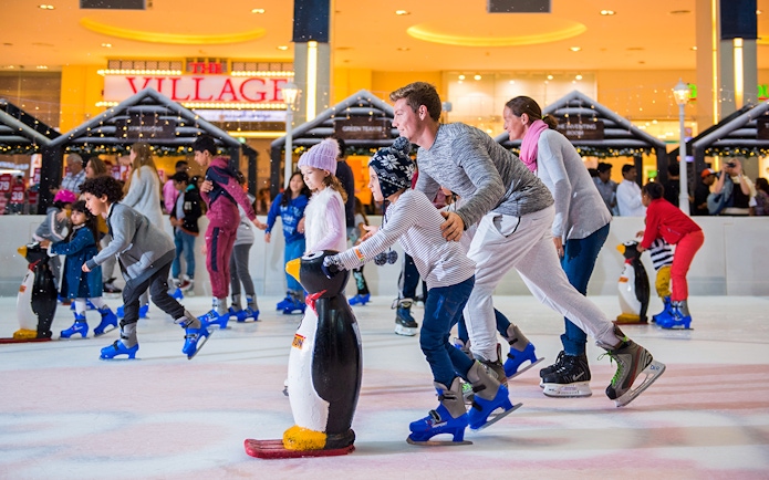 Families ice skating at Dubai Ice Rink with penguin skating aids.