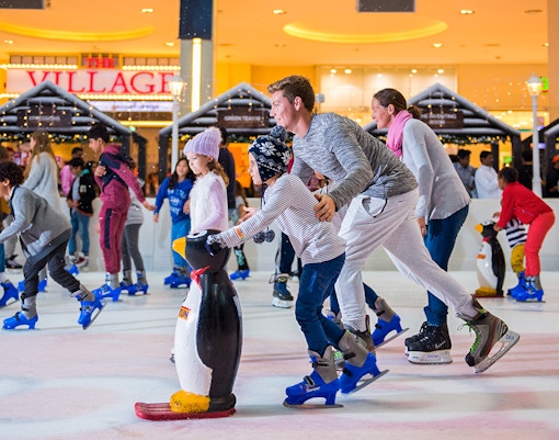 Families ice skating at Dubai Ice Rink with penguin skating aids.
