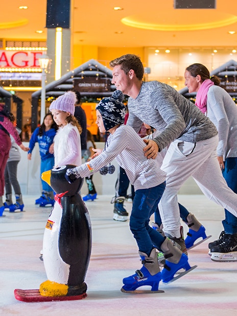 Families ice skating at Dubai Ice Rink with penguin skating aids.