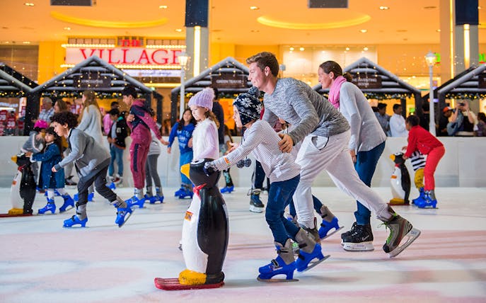 Families ice skating at Dubai Ice Rink with penguin skating aids.