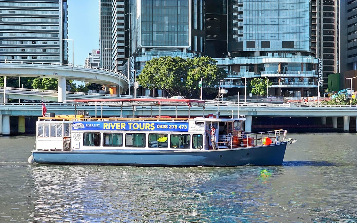 Boat cruising on Brisbane River with city buildings in the background.