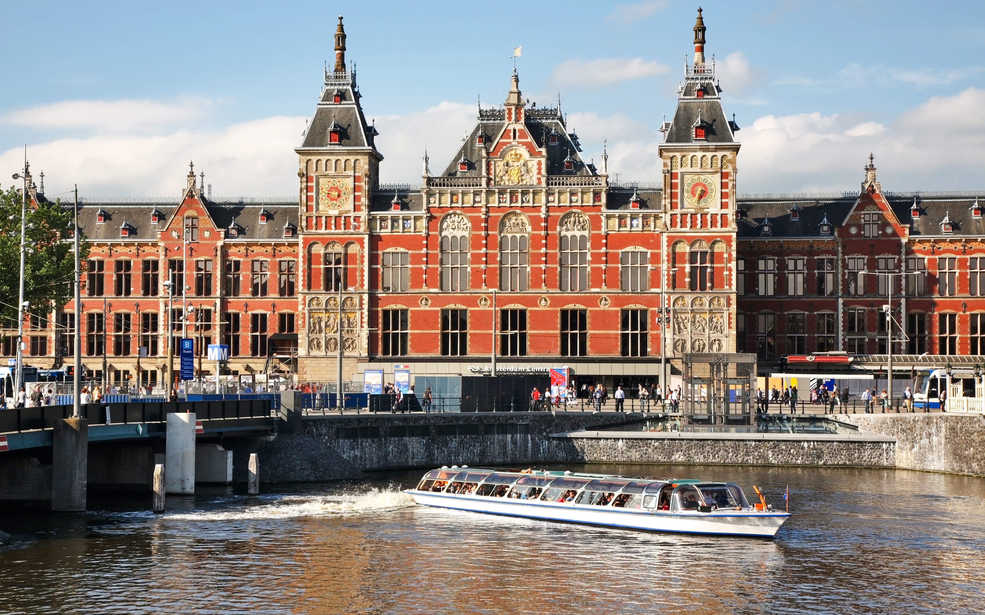 Cruise boat passing in front of Amsterdam Central Station under a bridge.