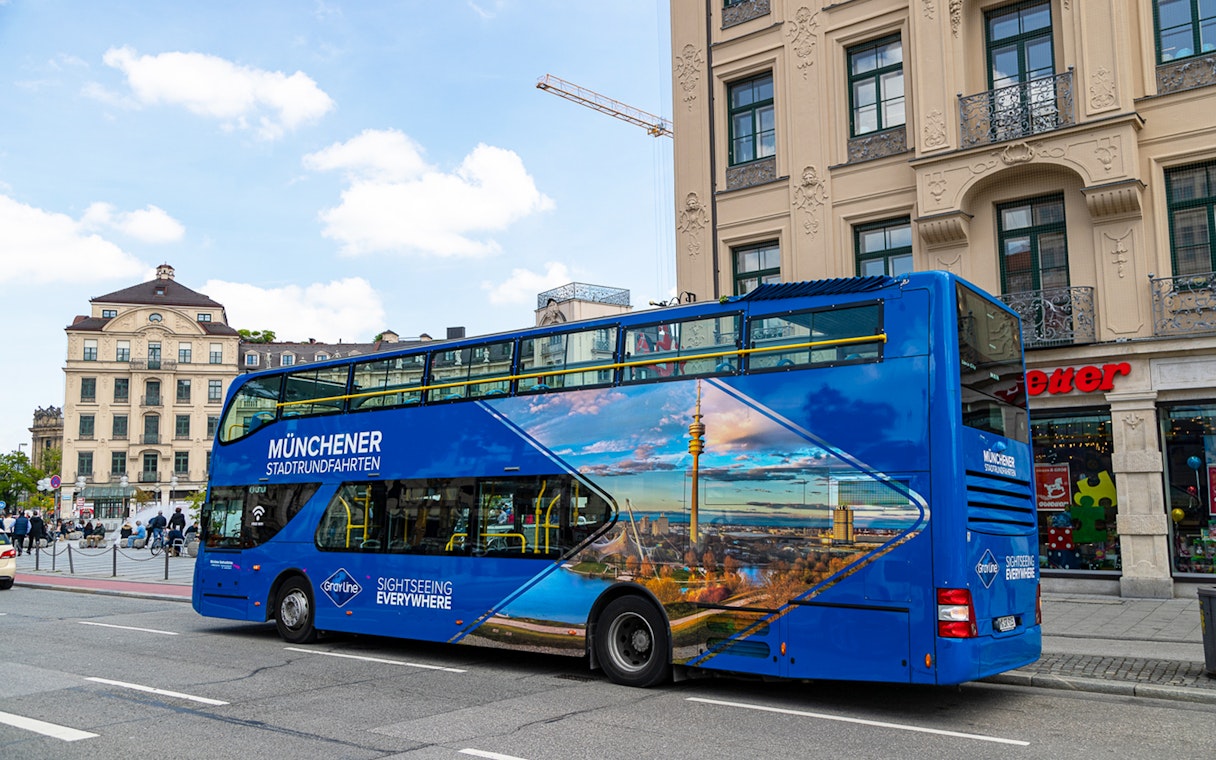 Blue double-decker tour bus in Munich city center, promoting city and FC Bayern Munich Arena tours.