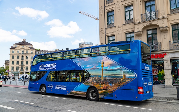Blue double-decker tour bus in Munich city center, promoting city and FC Bayern Munich Arena tours.