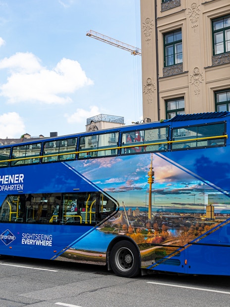 Blue double-decker tour bus in Munich city center, promoting city and FC Bayern Munich Arena tours.