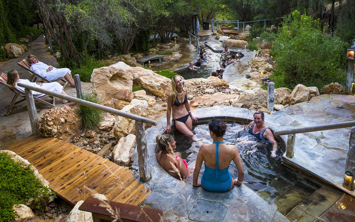 Visitors relaxing in geothermal pools at Peninsula Hot Springs, surrounded by natural rock and greenery.