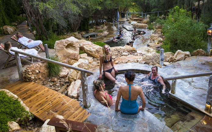 Visitors relaxing in geothermal pools at Peninsula Hot Springs, surrounded by natural rock and greenery.