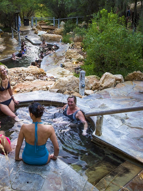 Visitors relaxing in geothermal pools at Peninsula Hot Springs, surrounded by natural rock and greenery.