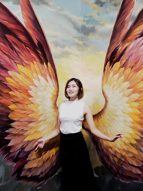 Person posing with angel wings mural at Art in Paradise Pattaya.