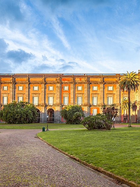 Courtyard of Capodimonte Museum with palm trees and historic building in Naples, Italy.