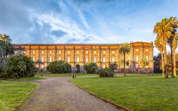 Courtyard of Capodimonte Museum with palm trees and historic building in Naples, Italy.