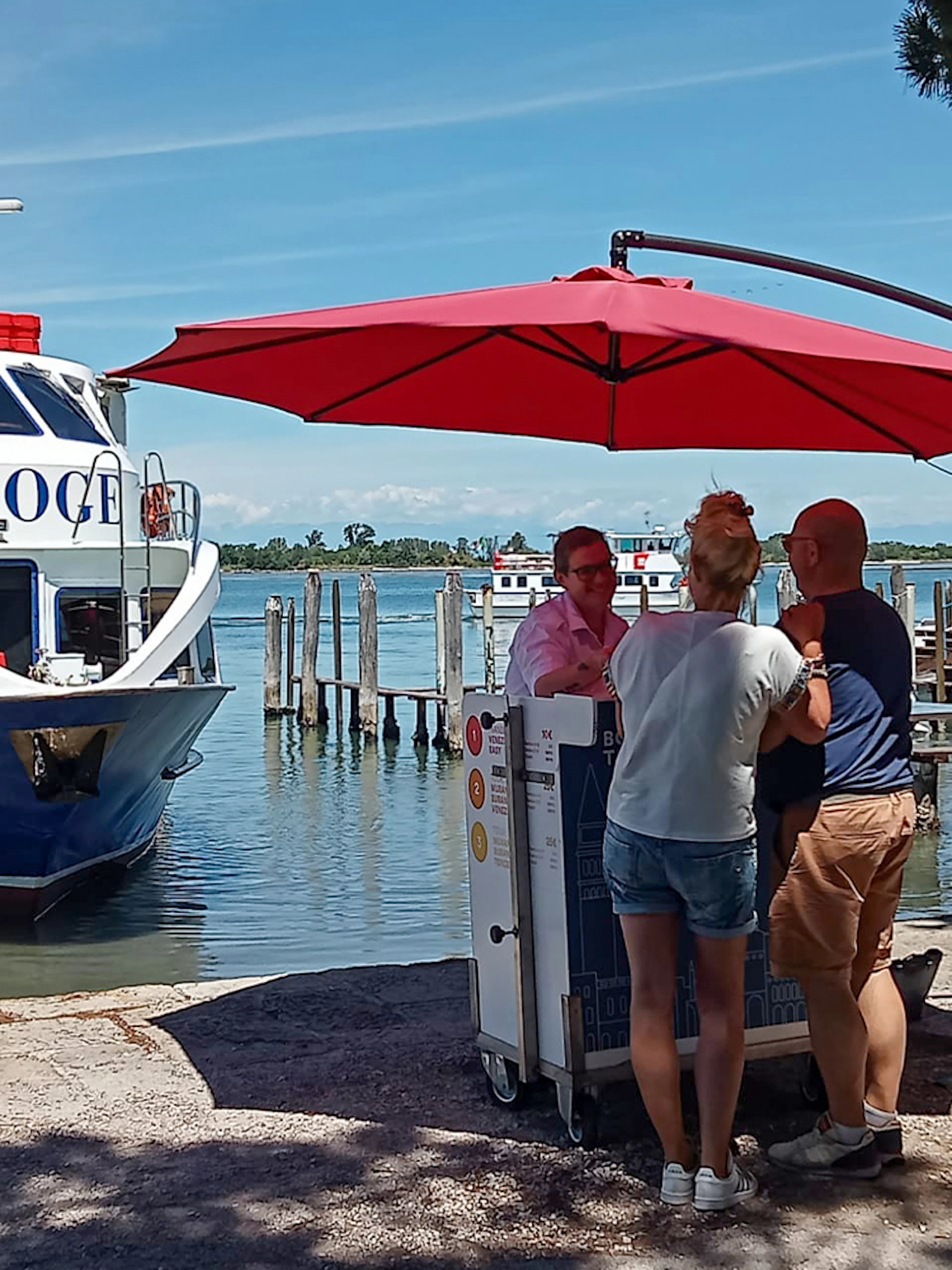 Boat docked at Punta Sabbioni with people under a red umbrella, Venice tour to Murano and Burano.