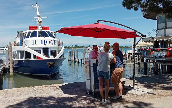 Boat docked at Punta Sabbioni with people under a red umbrella, Venice tour to Murano and Burano.