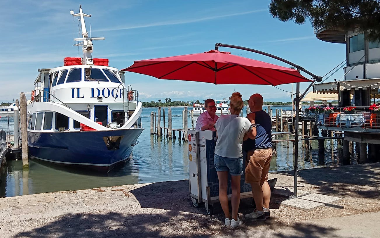 Boat docked at Punta Sabbioni with people under a red umbrella, Venice tour to Murano and Burano.