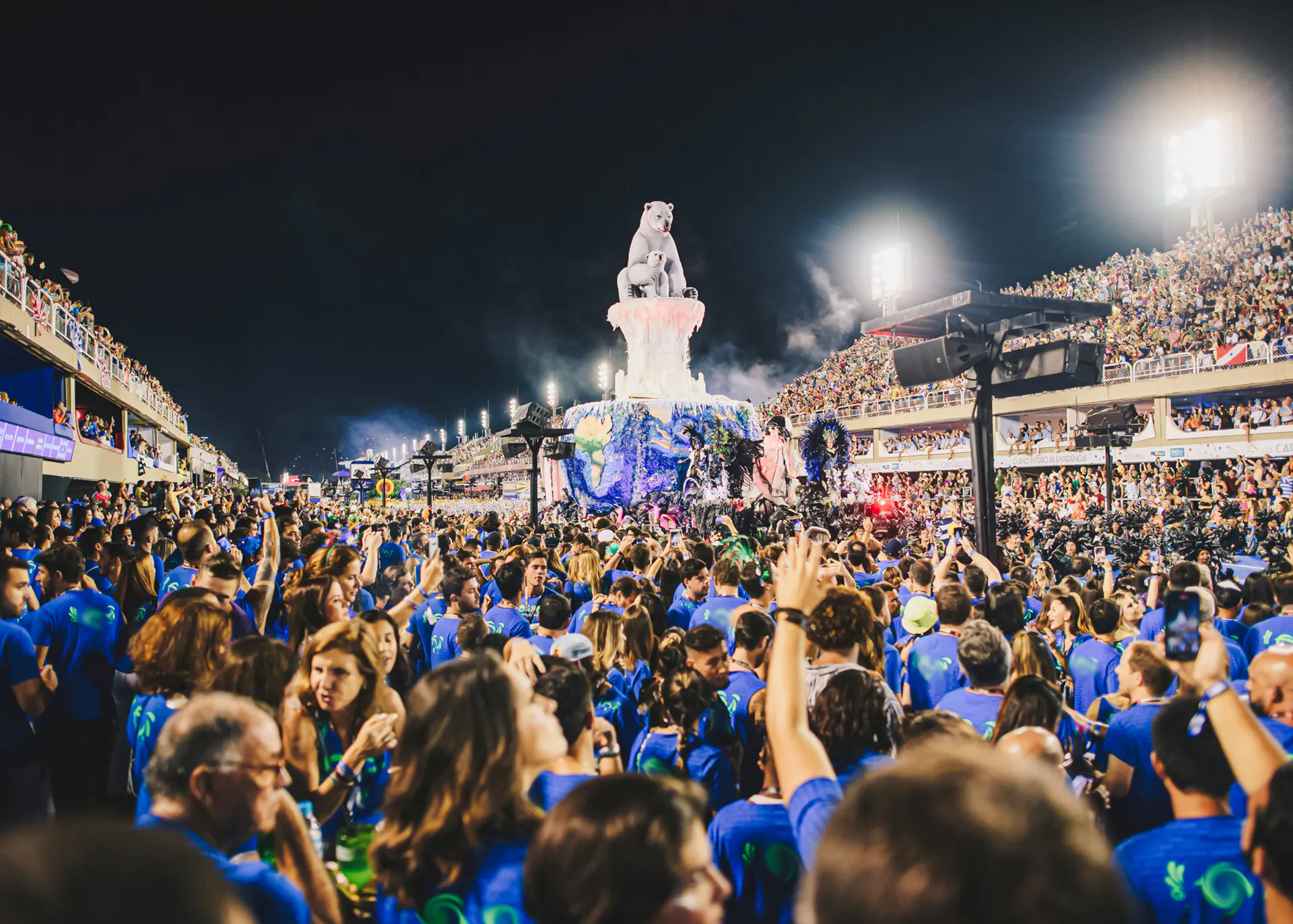 Crowd enjoying Rio Carnival parade at Marquês de Sapucaí, Rio de Janeiro, with vibrant floats and performers.