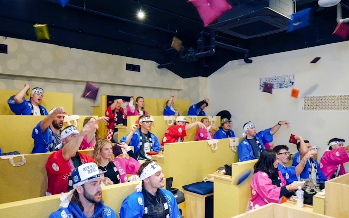 Tourists in colorful attire enjoying a sumo show in Ginza viewing arena.