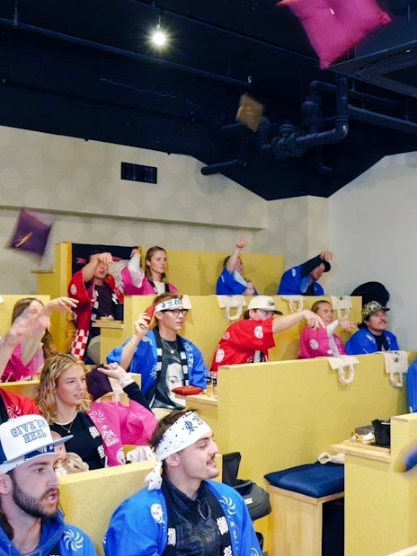 Tourists in colorful attire enjoying a sumo show in Ginza viewing arena.