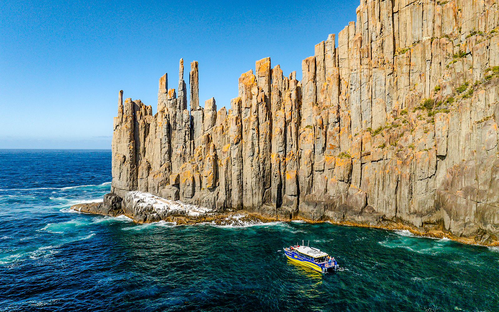 Boat cruising near Cape Raoul cliffs, Tasmania.