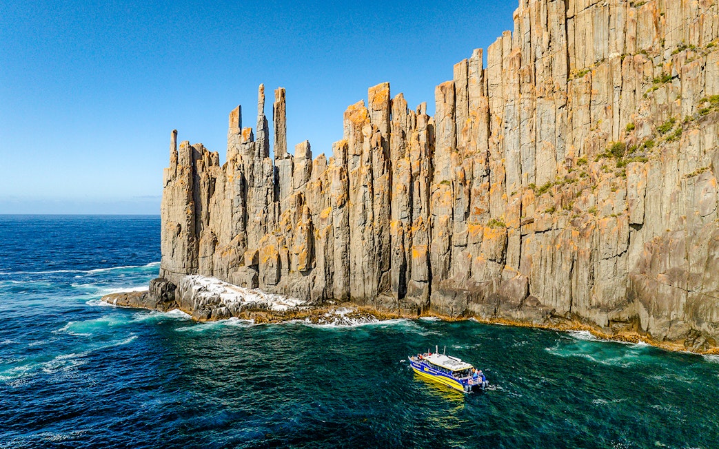 Boat cruising near Cape Raoul cliffs, Tasmania.