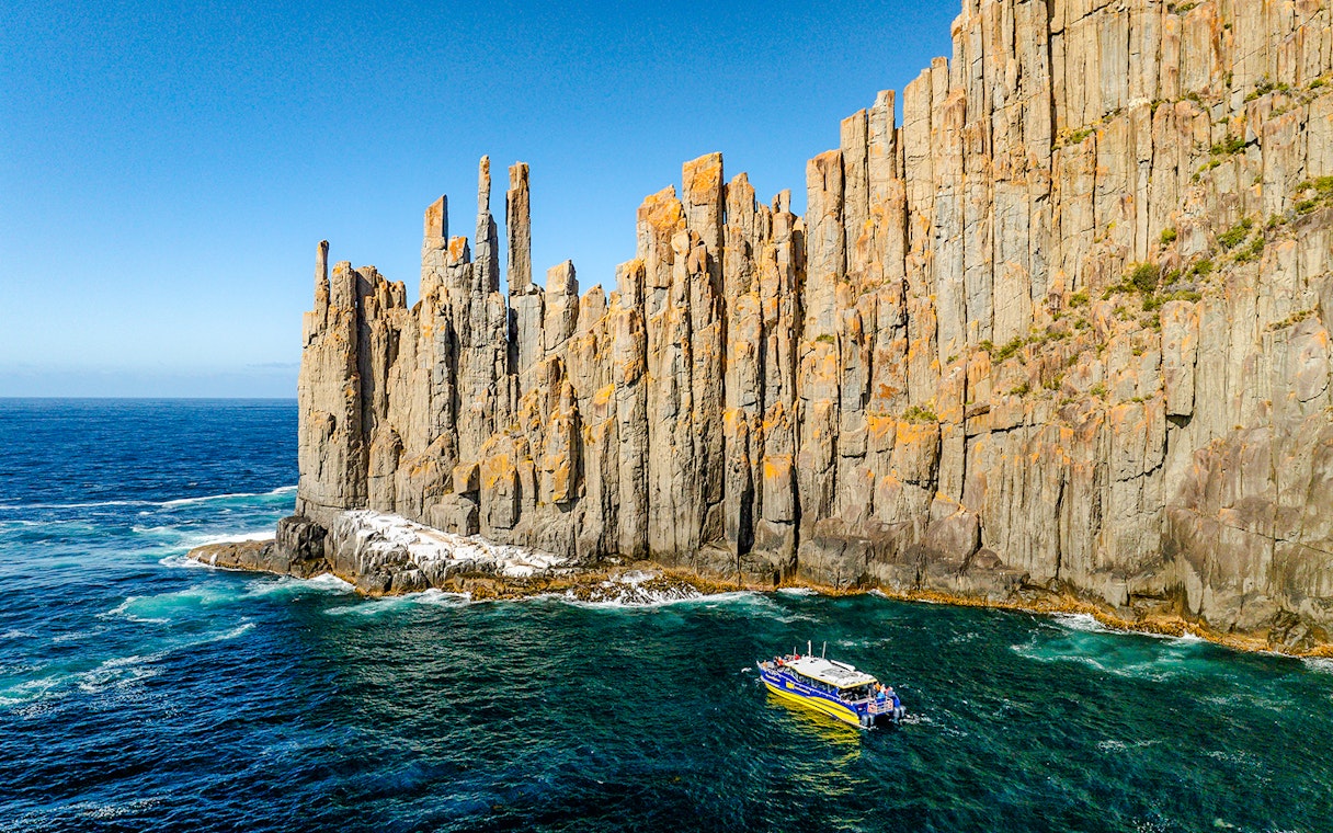 Boat cruising near Cape Raoul cliffs, Tasmania.