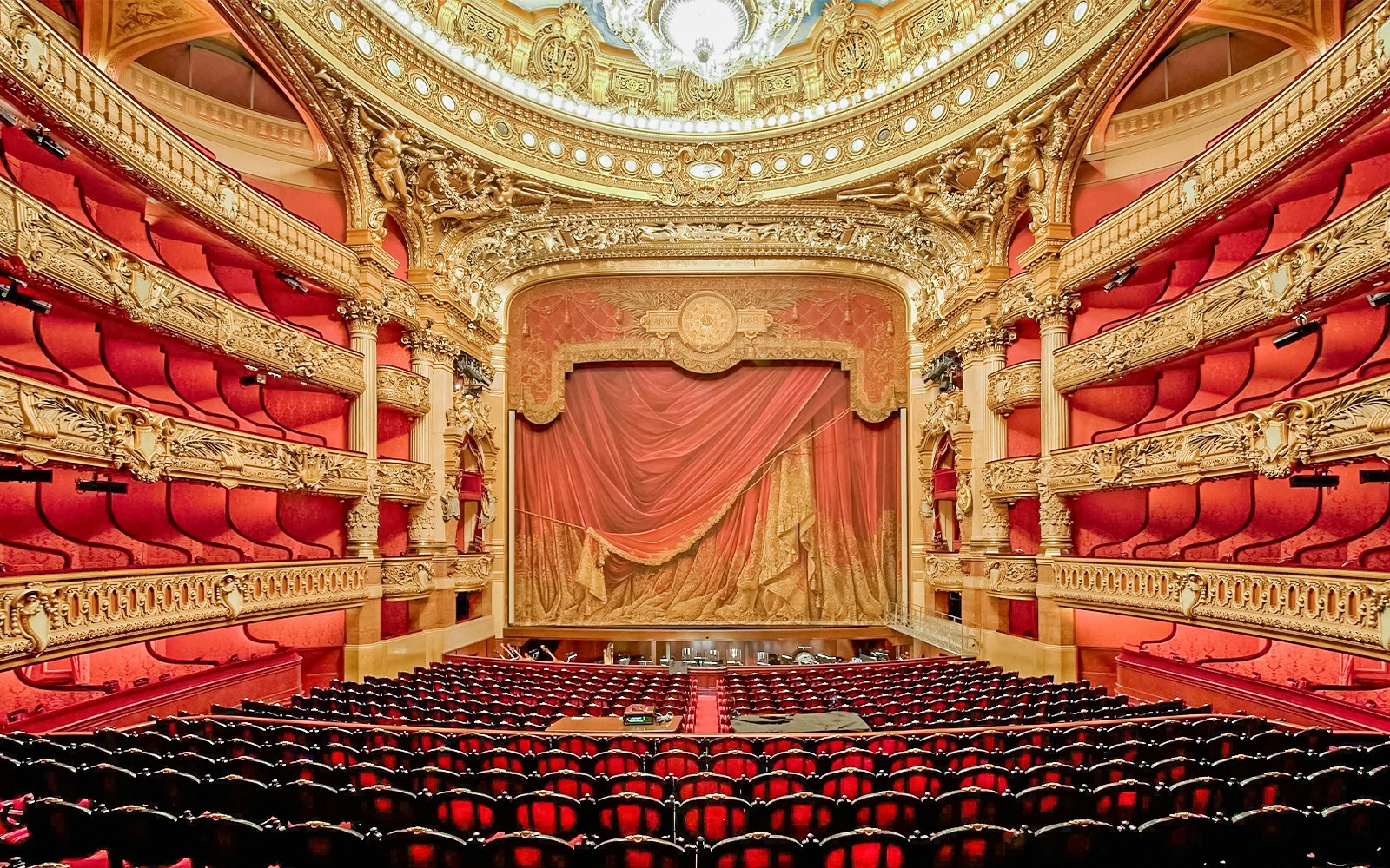 Der prunkvolle Innenraum der Opéra Garnier in Paris mit roten Sitzen, goldenen Verzierungen und einem geschlossenen Vorhang