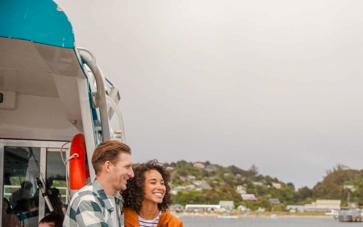 Couple enjoying the view on Stewart Island Ferry, New Zealand coast in background.