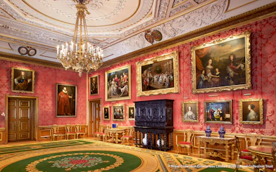 Windsor Castle interior with ornate ceiling, chandelier, and paintings on red walls.