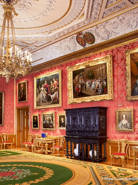 Windsor Castle interior with ornate ceiling, chandelier, and paintings on red walls.