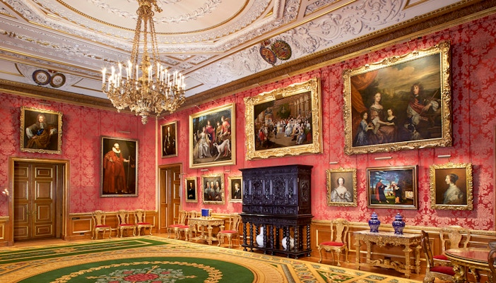 Windsor Castle interior with ornate ceiling, chandelier, and paintings on red walls.