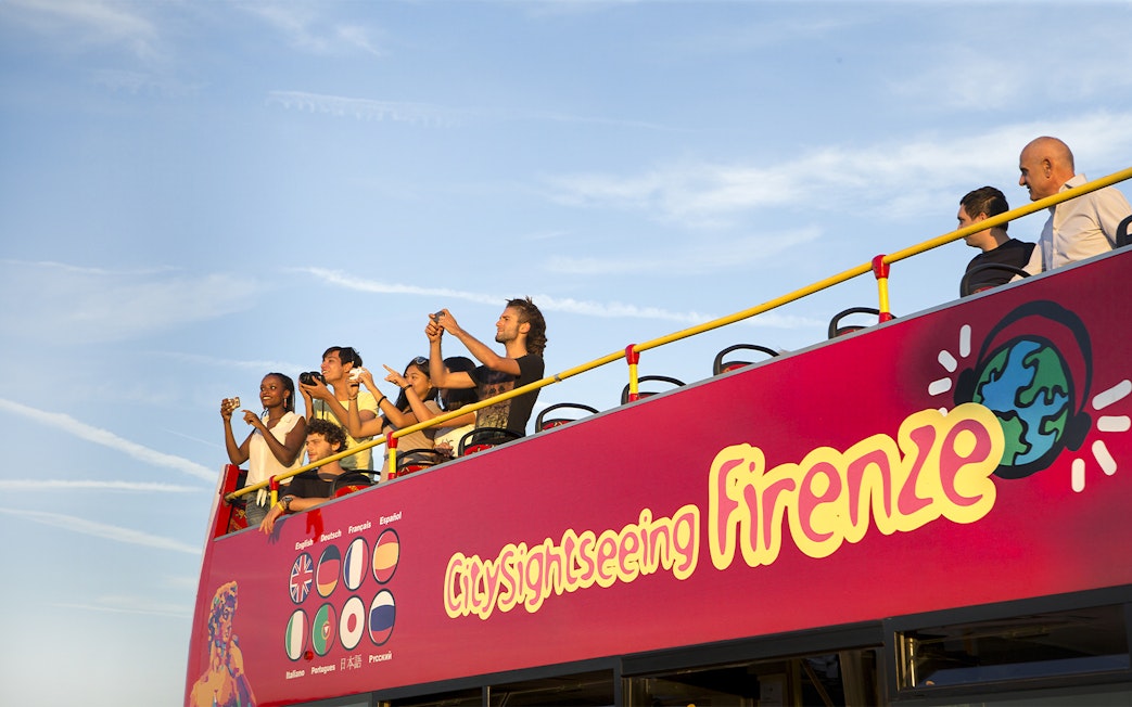 Tourists on open deck of sightseeing bus in Florence, capturing views.