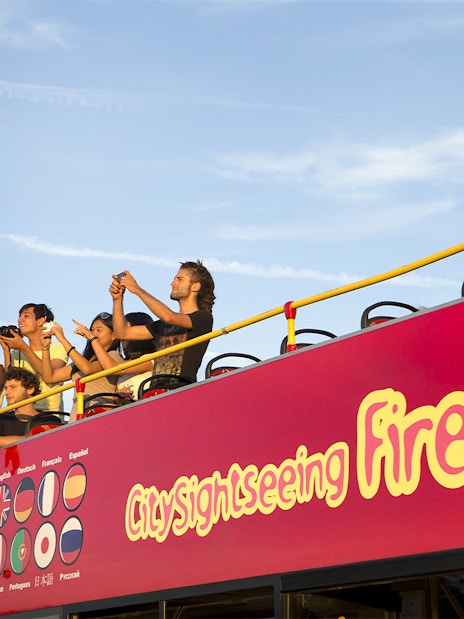 Tourists on open deck of sightseeing bus in Florence, capturing views.