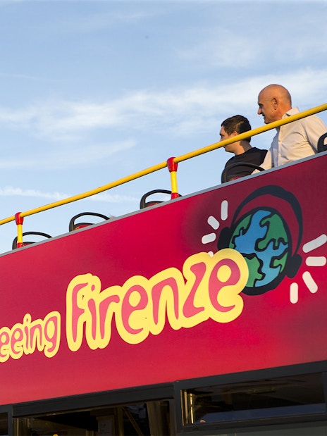 Tourists on open deck of sightseeing bus in Florence, capturing views.