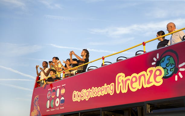 Tourists on open deck of sightseeing bus in Florence, capturing views.