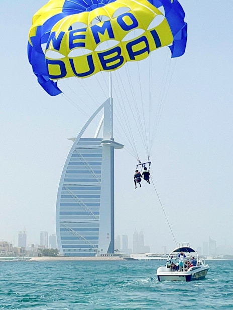 Parasailing near Burj Al Arab in Dubai with a boat on the water.