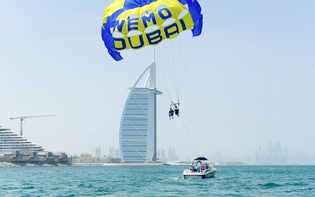 Parasailing near Burj Al Arab in Dubai with a boat on the water.