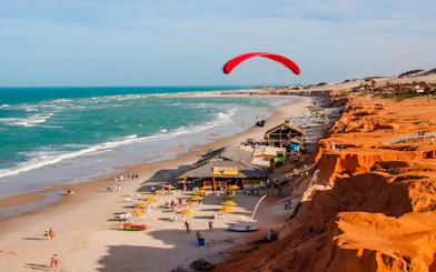 Paragliding over colorful cliffs and beach at Canoa Quebrada, Brazil.