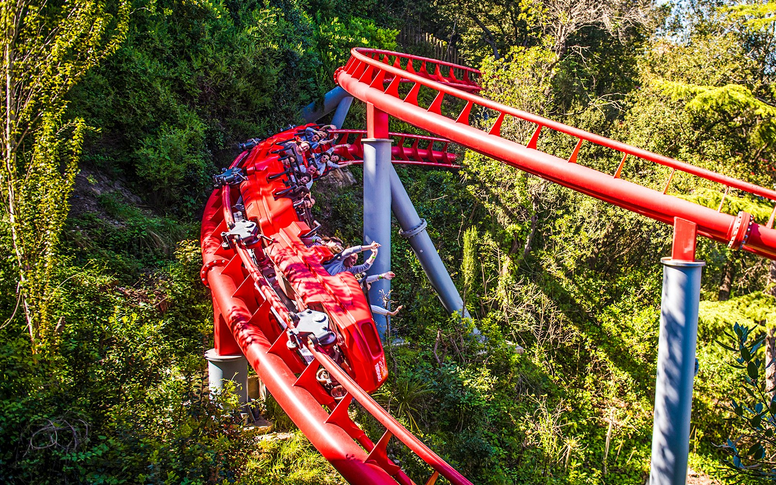 Red roller coaster at Tibidabo Amusement Park, Barcelona, surrounded by trees.