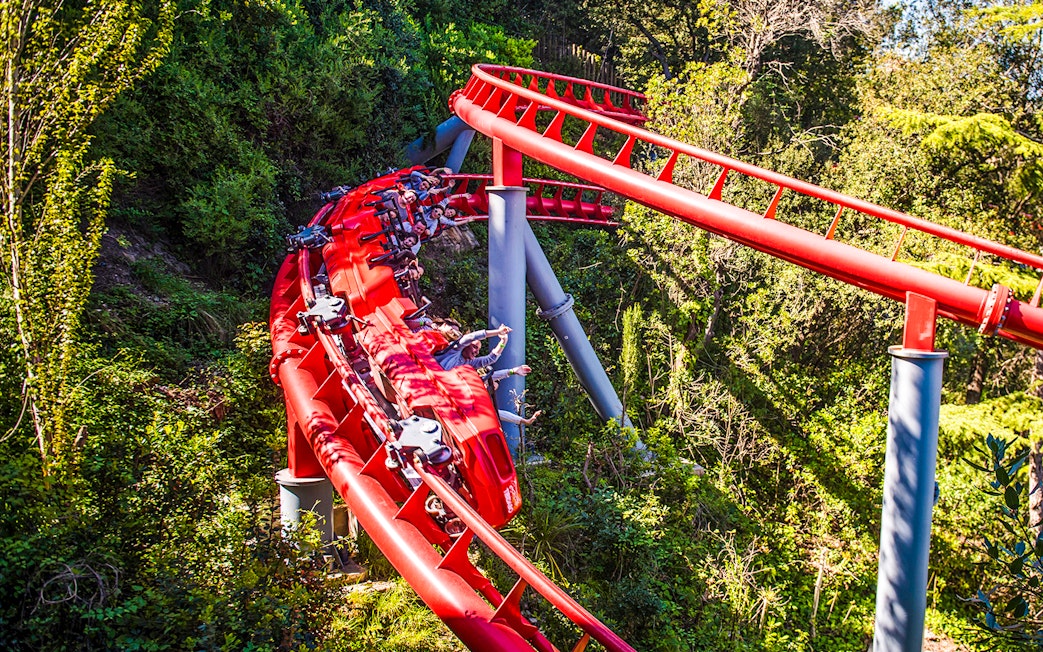 Red roller coaster at Tibidabo Amusement Park, Barcelona, surrounded by trees.
