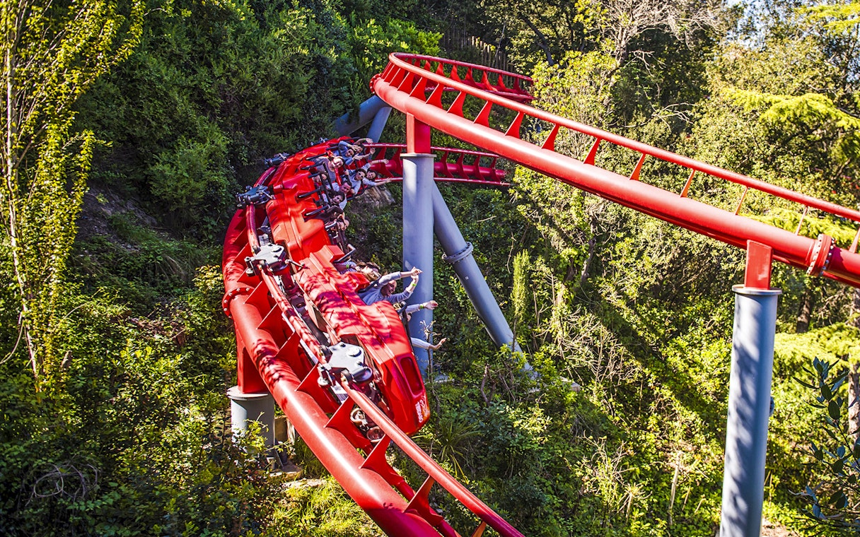 Red roller coaster at Tibidabo Amusement Park, Barcelona, surrounded by trees.