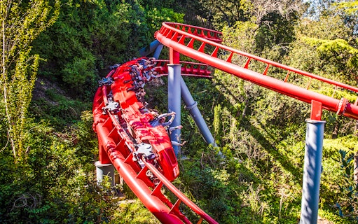 Red roller coaster at Tibidabo Amusement Park, Barcelona, surrounded by trees.