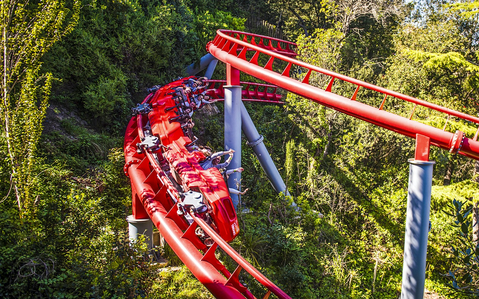 Red roller coaster at Tibidabo Amusement Park, Barcelona, surrounded by trees.