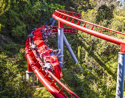 Red roller coaster at Tibidabo Amusement Park, Barcelona, surrounded by trees.