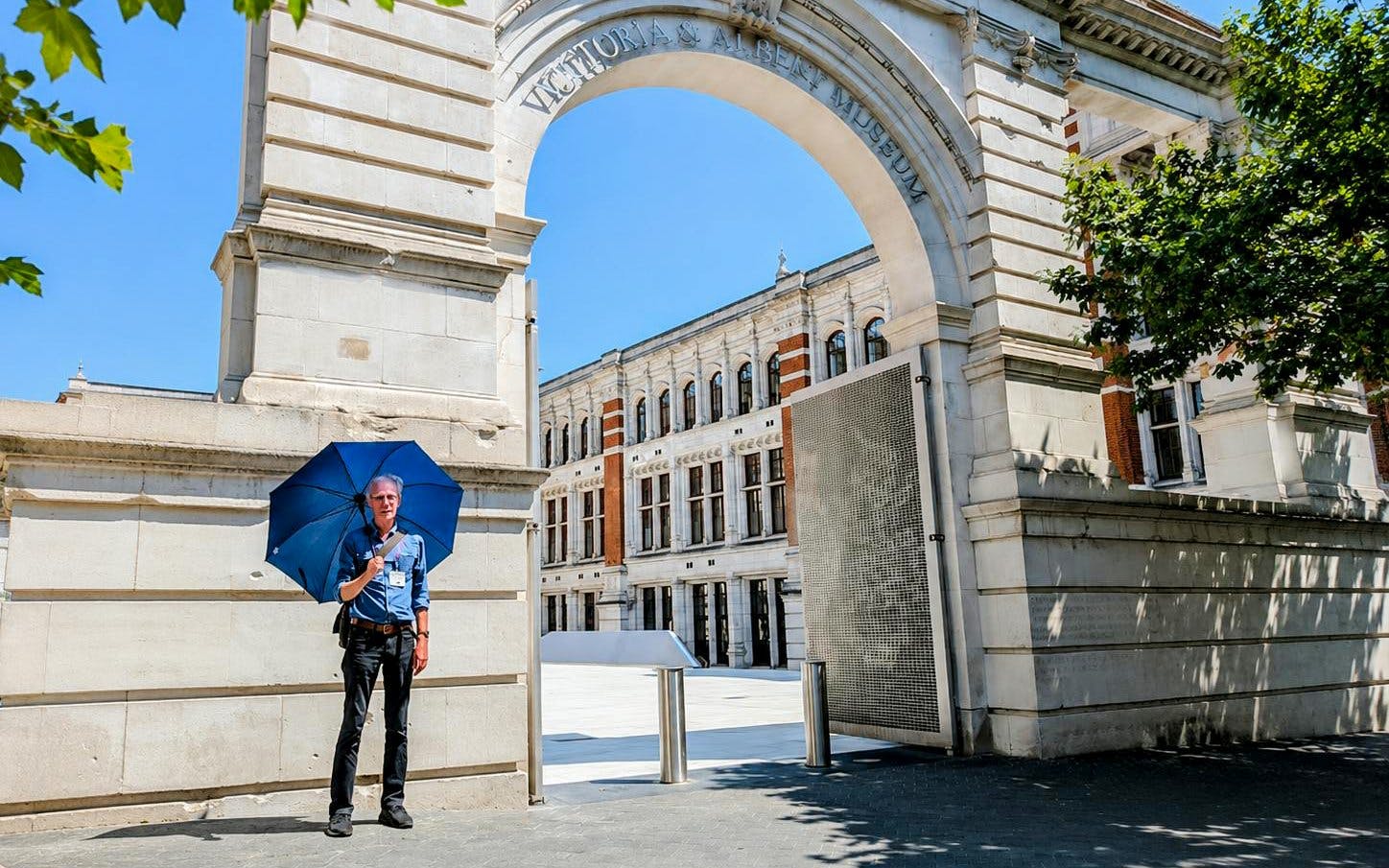 Man with blue umbrella at Victoria and Albert Museum entrance, London.