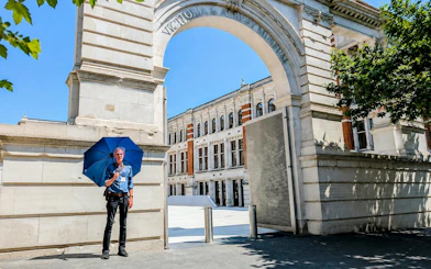 Man with blue umbrella at Victoria and Albert Museum entrance, London.
