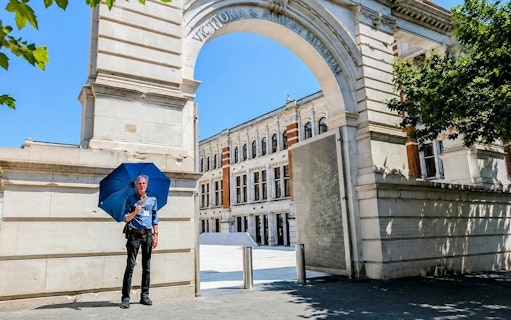 Man with blue umbrella at Victoria and Albert Museum entrance, London.