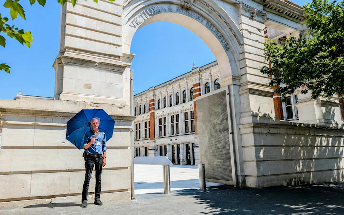 Man with blue umbrella at Victoria and Albert Museum entrance, London.