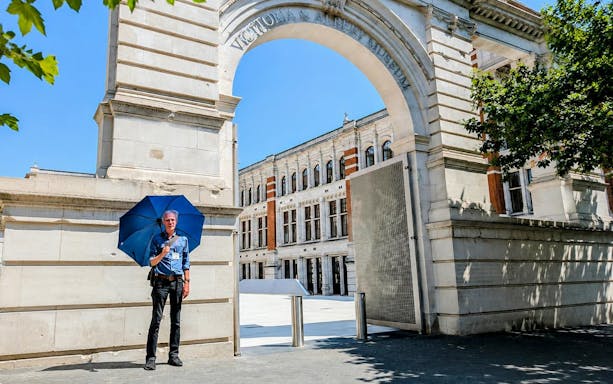Man with blue umbrella at Victoria and Albert Museum entrance, London.